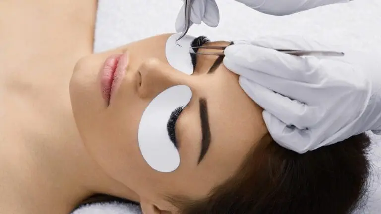 Edgemont A close-up of a woman receiving eyelash extensions at the waxing studio in Edgemont Village, with white pads under her eyes and a professional using tweezers to apply the lashes. North Vancouver