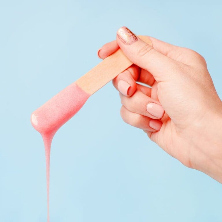 Edgemont A hand with painted nails holds a wooden stick, lifting a stretchy pink substance, against a plain light blue background. North Vancouver